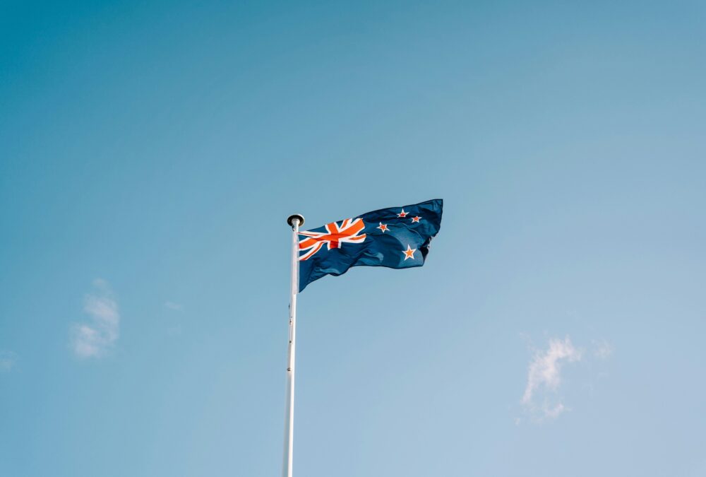 A low-angle wide shot of the New Zealand flag against a blue sky background.